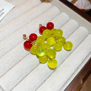 Close-up of red and yellow resin grape tassel earrings on beige velvet jewelry box tray
