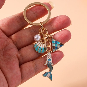 Detail of mermaid and shell enamel charms with a pearl on a golden keychain ring