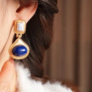 Detail of vintage gold earrings with marble and blue stone worn by a model