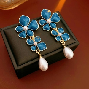 Macro detail of blue enamel flower earrings with pearls and gold-plated petal edges