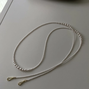 Detail of elegant French long pearl chain with gradient white pearls and gold metal hooks