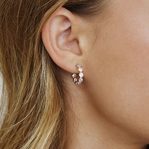 Macro shot of rose gold C-shaped hoop earrings with zircon pavé setting on a model