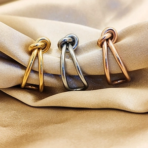 Detailed view of 18K gold, silver, and rose gold knotted rings on champagne satin fabric