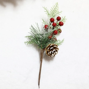 Artificial Christmas cedar branch with red berries and snowy pine cones on white fur