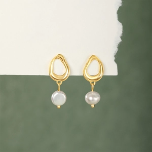 Macro detail of gold irregular hoop earrings featuring elegant white hanging pearls