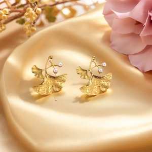 Golden ginkgo leaf earrings with pearls on elegant gold silk fabric background