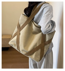 Side view of large khaki canvas tote bag with brown straps worn on a model's shoulder