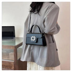 Détail d'un sac bandoulière en cuir noir avec une boucle en cristal étincelante sur le rabat