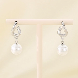 Detailed view of silver bow earrings with pearl drops displayed on a minimalist jewelry stand