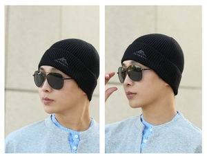 Close-up detail of black knitted beanie featuring mountain logo embroidery on a model