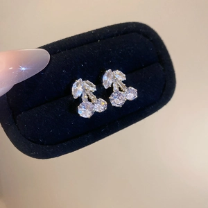 Detailed view of silver cherry stud earrings with clear zircons on black velvet box