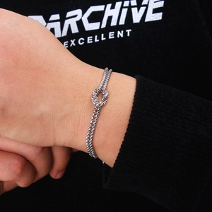 Close-up of a silver stainless steel knot design bracelet worn on a wrist against black