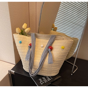 Detail of beige woven tote bag with colorful pom-poms and striped ribbon handle