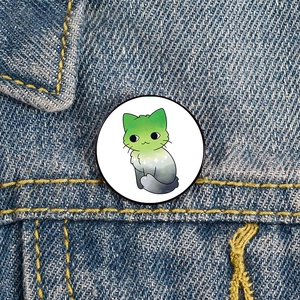 Cartoon cat enamel pin with green gradient shown pinned on a blue denim jacket