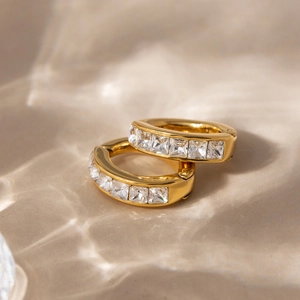 Orecchini huggie in acciaio placcato oro 18K con zirconi quadrati su sfondo ondulato