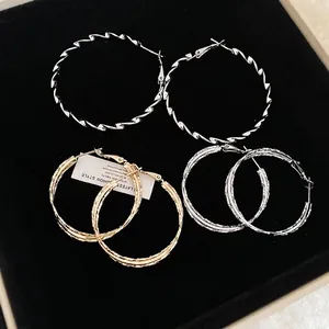 Three pairs of stylish gold and silver twisted geometric hoop earrings on black velvet
