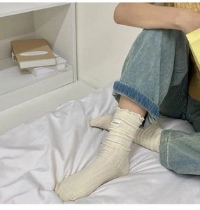 Close-up of cream ruffled edge socks with vertical stripes worn in a cozy bedroom setting