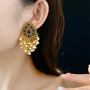 Détail de boucles d'oreilles vintage dorées avec gemmes noires et pompons de perles