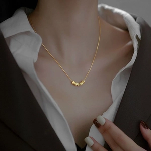 Elegant gold necklace with five small beads on a chain, worn with a white shirt and blazer