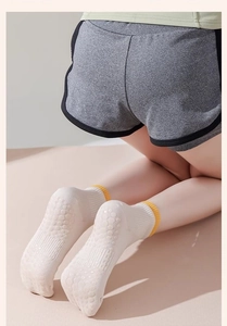 Detail von beigen Yoga-Socken mit gelben Streifen und rutschfester Sohle auf Matte