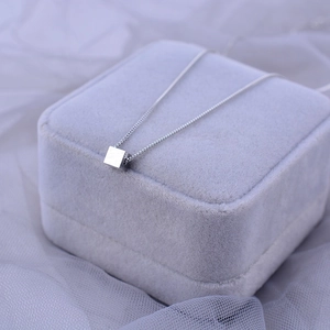 Macro detail of a silver cube pendant on a fine box chain over a soft purple jewelry box