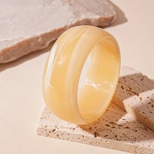 Macro shot of wide marble-patterned resin bangle resting on natural travertine stone