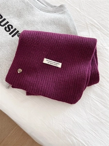 Dettaglio sciarpa in maglia viola con etichetta in tessuto e bottone in metallo rétro