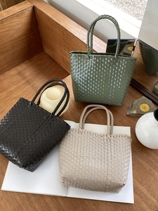 Detailed view of woven straw tote bags in olive green, black, and beige on wood background