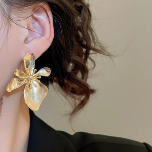 Close-up of a large gold metallic flower earring worn by a model in an elegant style