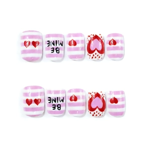 Detail view of pink and white Valentine's Day press-on nails with hearts and BE MINE text