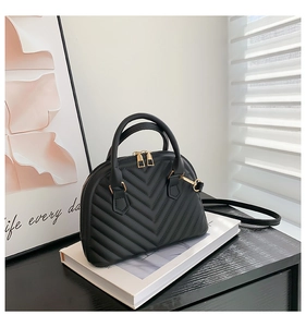 Detail view of black quilted shell handbag with golden double zippers and curved handle