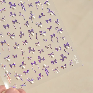 Macro shot of 3D iridescent laser purple bow nail stickers with white pearl accents
