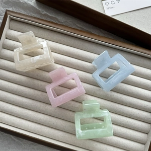 Close-up of four pastel marble hair claws in white, blue, pink and green on a display box