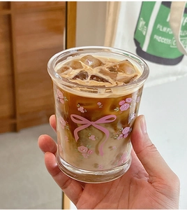 Gros plan d'une tasse en verre à motifs de fleurs roses et nœud remplie de café glacé