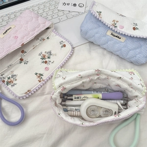 Quilted floral pencil cases with pom-pom trim shown next to stationery and laptop