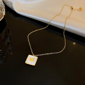 Detail of gold square necklace with white mother of pearl heart inlay on black mirror