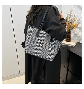 Detail of large houndstooth tote bag with leather handles shown on a black coat