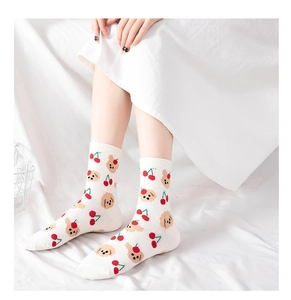 Detail showing white crew socks with cherry and teddy dog prints worn on a white bed