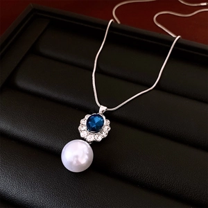 Macro detail of silver necklace featuring blue oval stone, rhinestone halo and large white pearl