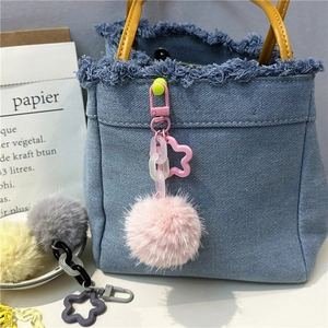 Close-up of colorful plush pom-pom charms with star clips on a blue denim bag