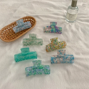 Seven medium marble pattern hair claws in assorted colors on a minimalist white fabric