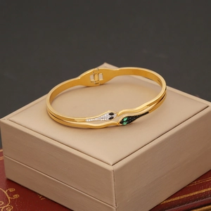 Detail of gold snake bangle featuring diamond-encrusted heads and green stone eyes