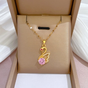 Detail of a gold swan necklace with pink gemstone and micro-inlaid crystals in a box