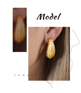 Detail of gold-plated cashew drop earrings with hammered texture on earlobe