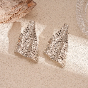 Détail macro de boucles d'oreilles argentées irrégulières avec texture froissée