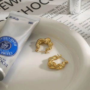 Macro shot of 18k gold plated twisted hoop earrings in a minimalist ceramic dish