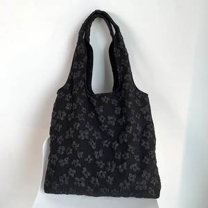Detailed view of black shoulder tote bag with 3D floral embossed texture on a chair