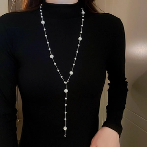 Detail of long gold-plated Y-necklace with irregular pearls on a black turtleneck top