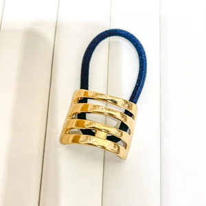 Close-up of blue elastic hair tie with tiered gold hollow metal ornament on white leather