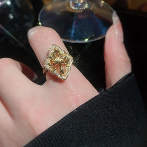 Detailed view of gold zircon flower ring with crystal bow on hand against dark backdrop